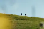 Zwei Personen gehen auf einem grünen Hügel unter klarem Himmel