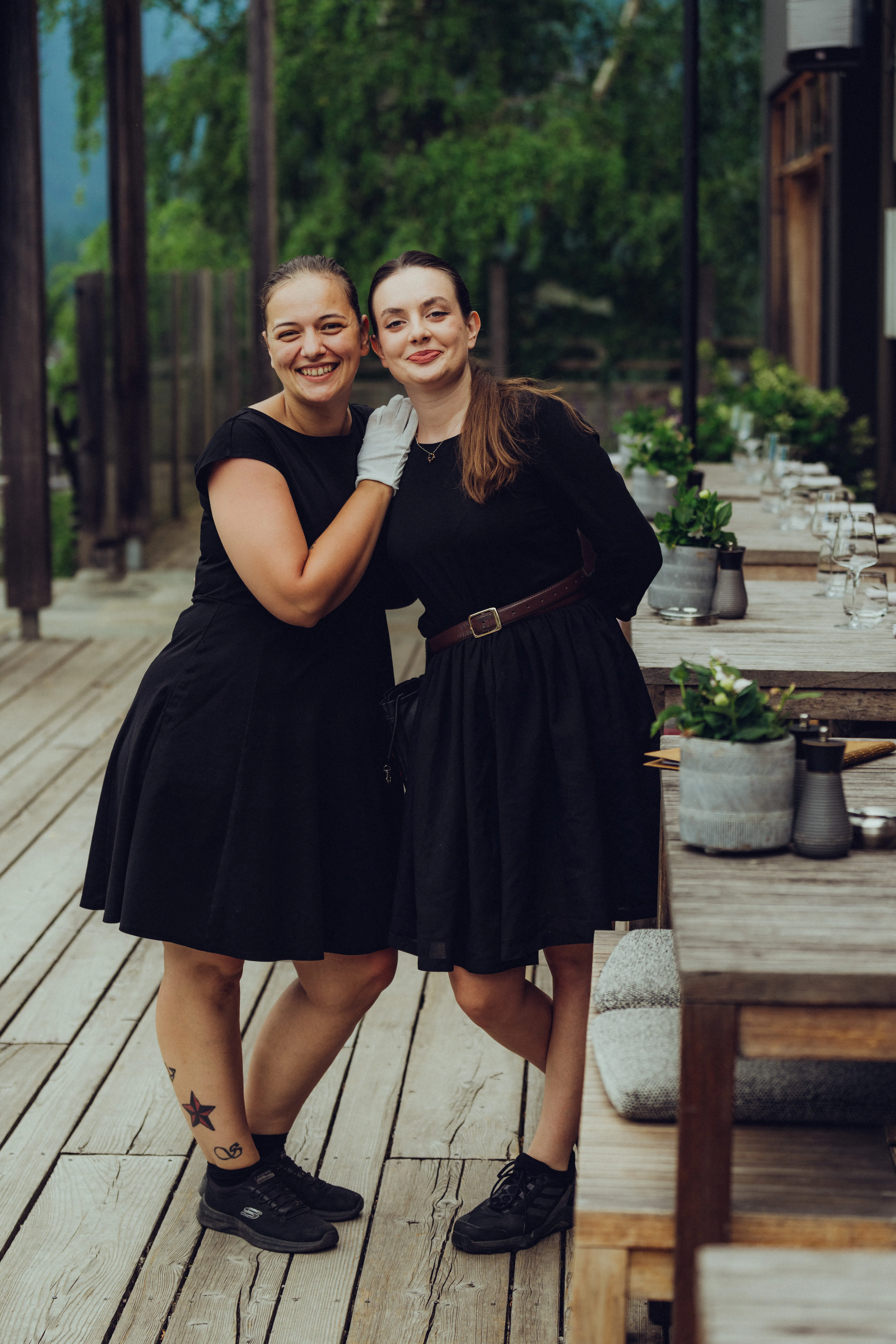 Zwei Frauen in schwarzen Kleidern posieren auf einer Holzterrasse